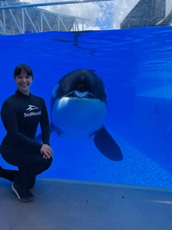 Kristin posing in front of an Orca in the aquarium