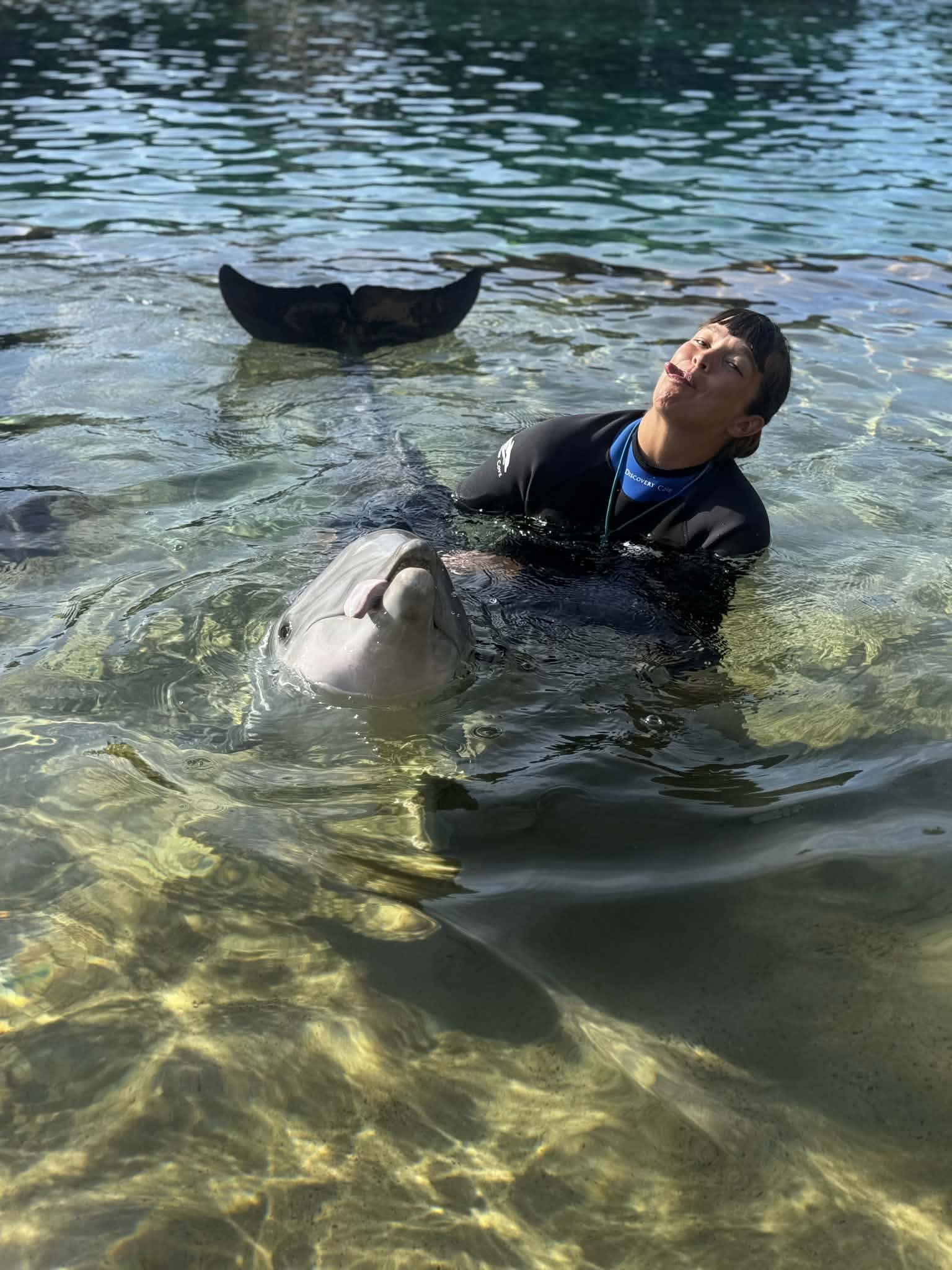 Kristin poses with her tongue sticking out next to a dolphin doing the same